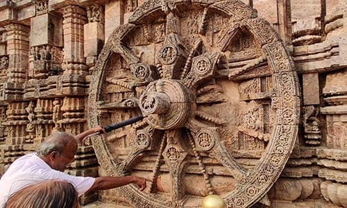 Large stone wheel with intricate designs on a temple wall, with a person touching it.
